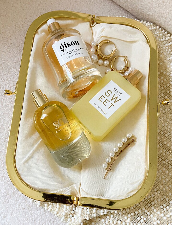 A purse lay open displaying a variety of fragrance sprays, oils, and pearl accessories. SHOP FRAGRANCE
