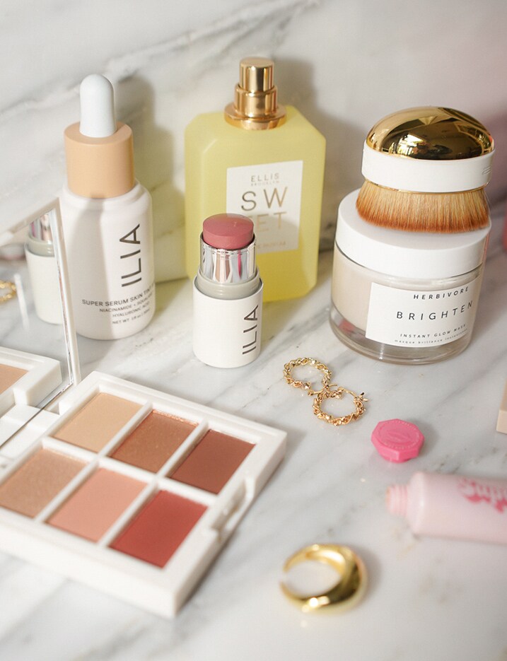 A variety of skincare and makeup products by clean beauty brands are displayed on a marble surface.