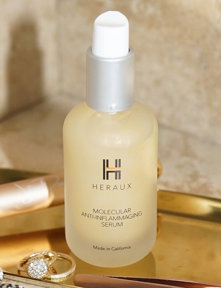 A bottle of Heraux Molecular Anti-inflammaging Serum sits on a brass tray. Brand Spotlight: Heraux. Shop Now.