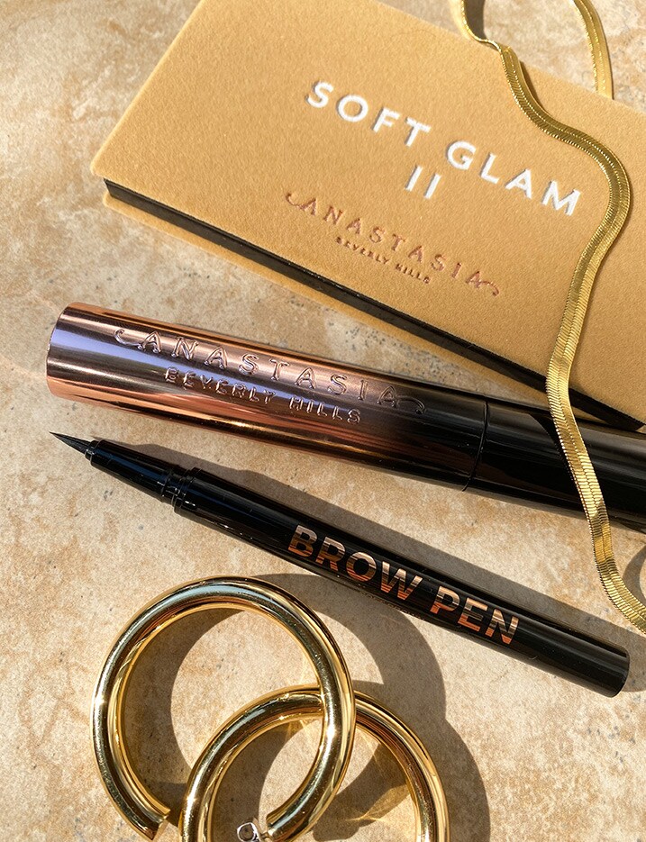 A folded cosmetic case titled Anastasia'S Soft Glam II sits on stone tiles with a few more Anastasia Beverly Hills eye brow products. Shop Makeup.