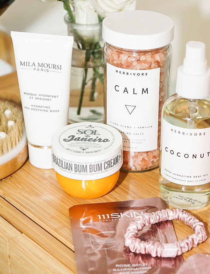 A variety of bath and body products like scrub salts and body lotion and oils sit on a wooden dresser. Shop Bath & Body.
