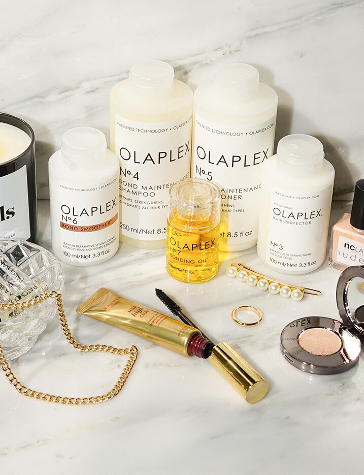 A variety of hair care products and accessories are displayed on a marble countertop featuring bottles from the haircare brand Olaplex. Shop Haircare.