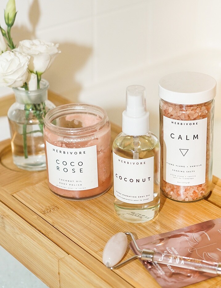 Herbivore body scrub, oil, and bath salts sit on top of a bamboo shelf. Shop Bath & Body.