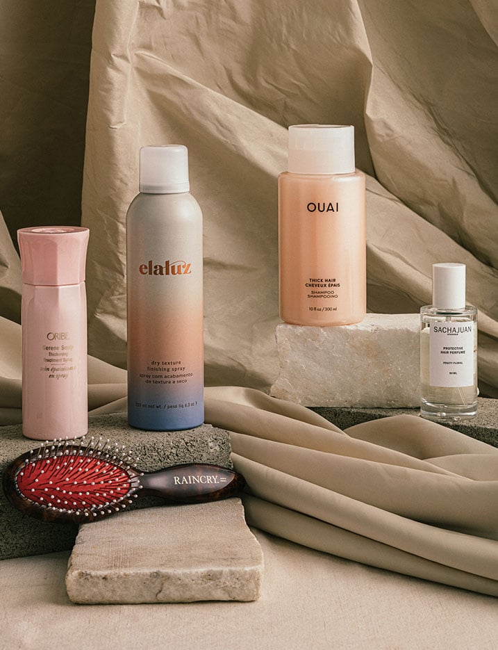 A variety of hair products sit on stones and draped cloth. Shop Hair.