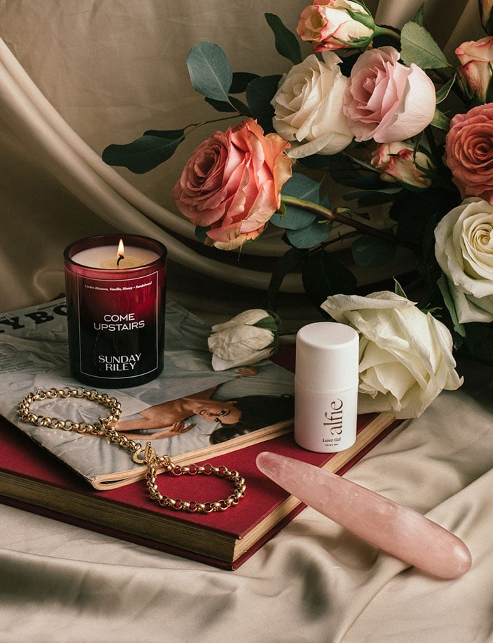 A variety of sexual wellness products sit on a table with roses and books. Shop Sexual Wellness.