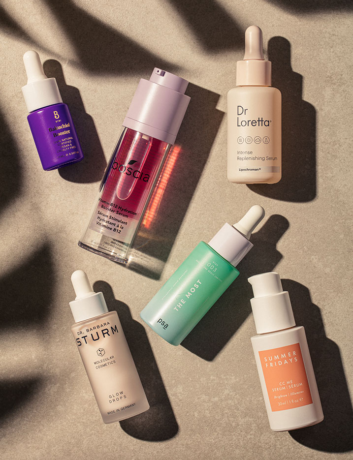 A variety of serum bottles lay on natural stone tiles. Shop Skin-Saving Serums.