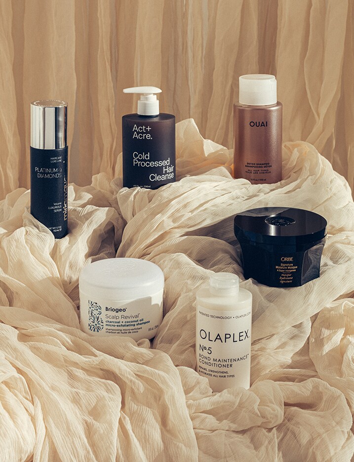 A variety of hair products displayed among gathered fabric. Shop Hair