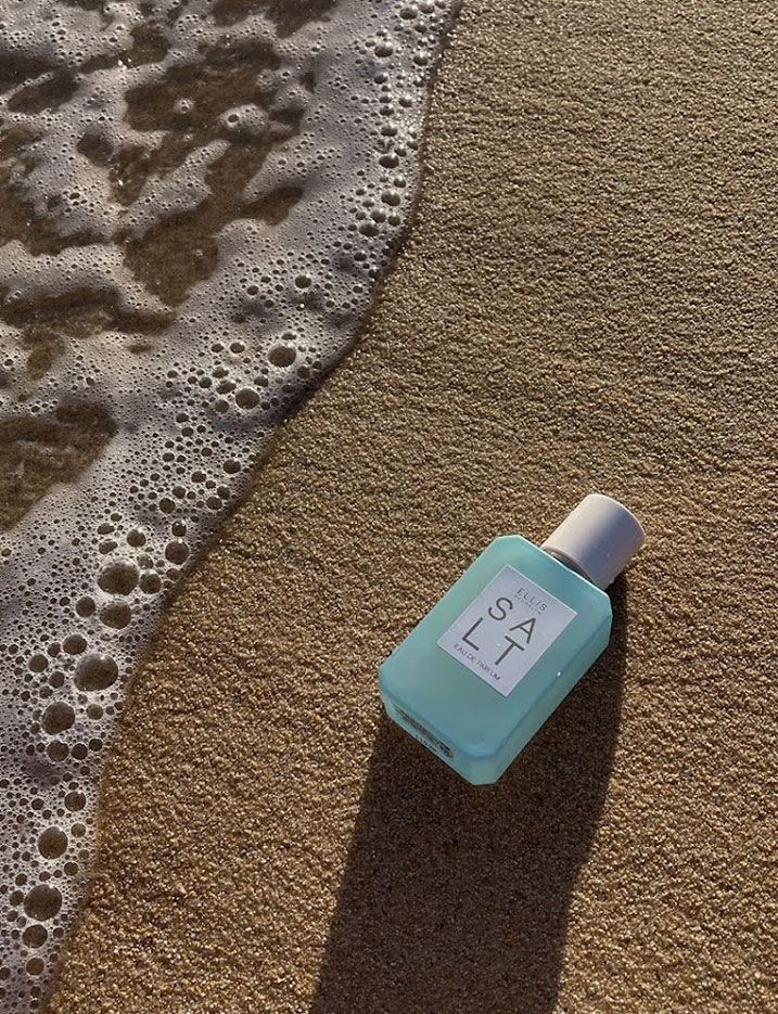 A sea-green bottle of Ellis Fragrance Salt Eau de Perfume lays in the wet sand by the ocean tide.