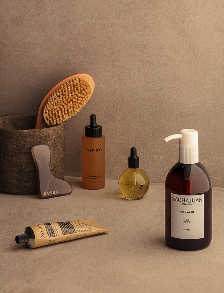 Bath and body products such as oils, soaps, creams and body brushes are displayed on a stone surface.