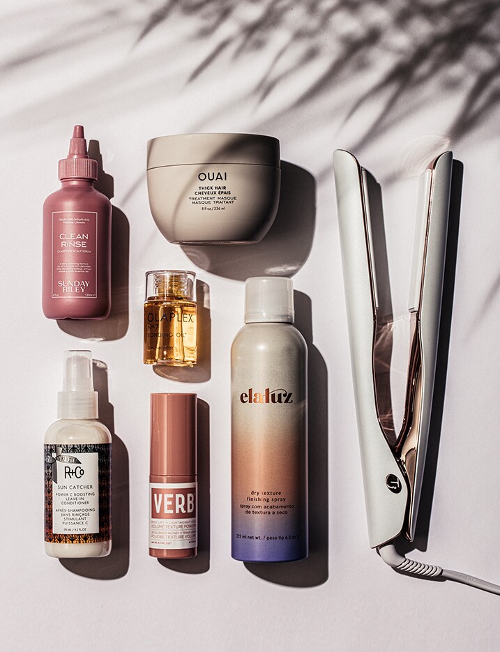 Hair care products and tools lined up under the shadow of a palm leaf.