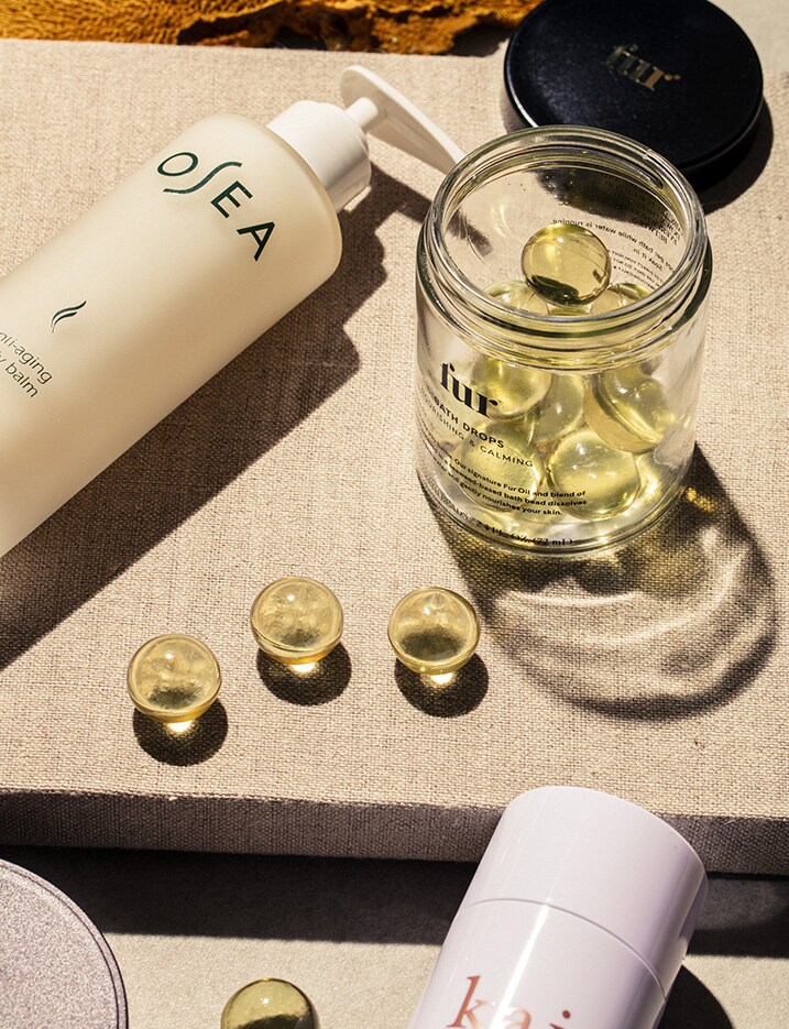 A variety of luxury body care products sit open on a linen top surface. Shop luxury body care.