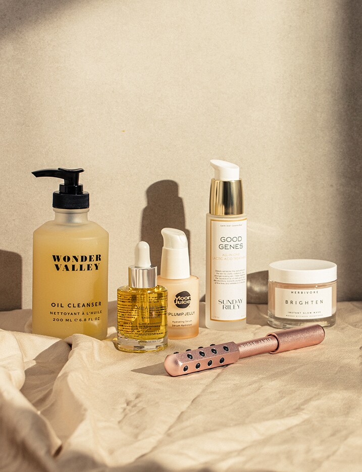 A variety of skincare products sit on a sand toned cloth against a sandstone wall.
