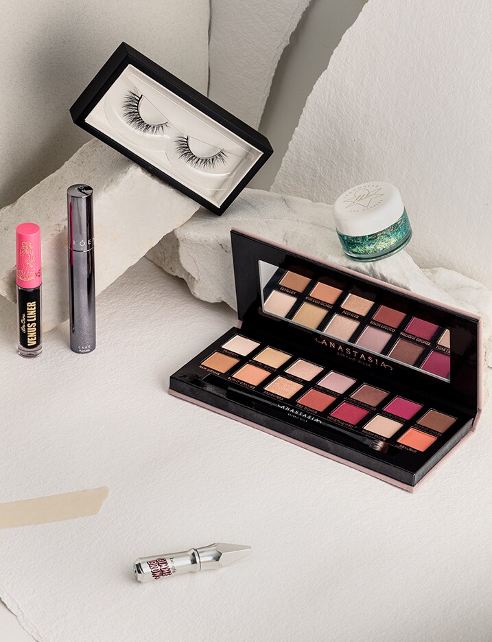 An open eyeshadow palette of colorful shades sits on a white table top with other eye makeup products.