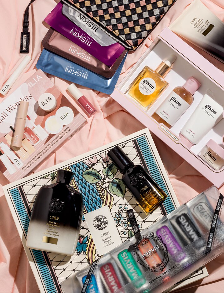 Gift sets from 111Skin, Gisou, Ilia, Oribe and Marvis lay open in a pink sheet, displaying the numerous products in each set.
