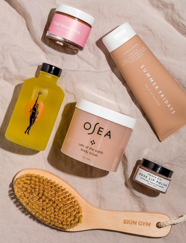 Bodycare products that provide skin hydration benefits and a bath scrub brush lay on a textured canvas cloth.