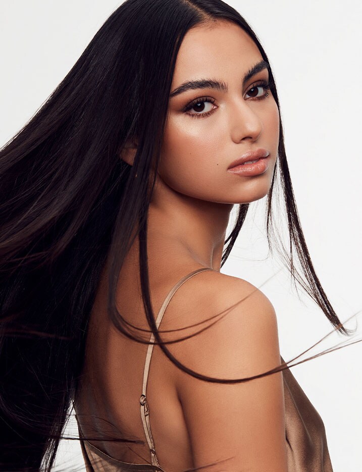 Model turns her head over her right shoulder, tossing her straight long, dark hair back with a few loose locks whipping around her shoulder.