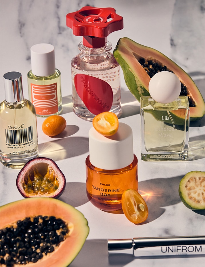 Bottles of fragrances playfully arranged with a variety of exotic fruits.