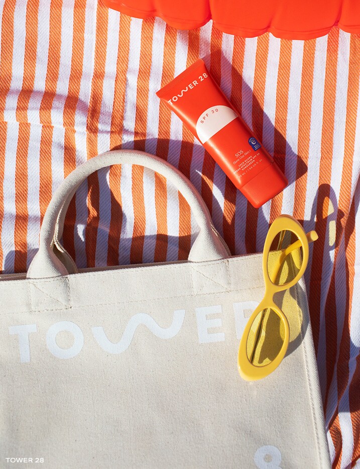 Tower 28's SOS Faceguard Broad Spectrum SPF 30 on a beach towel with a tote bag, sunglasses, and a pool tube.