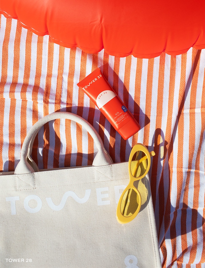 Tower 28's SOS Faceguard Broad Spectrum SPF 30 on a beach towel with a tote bag, sunglasses, and a pool tube.