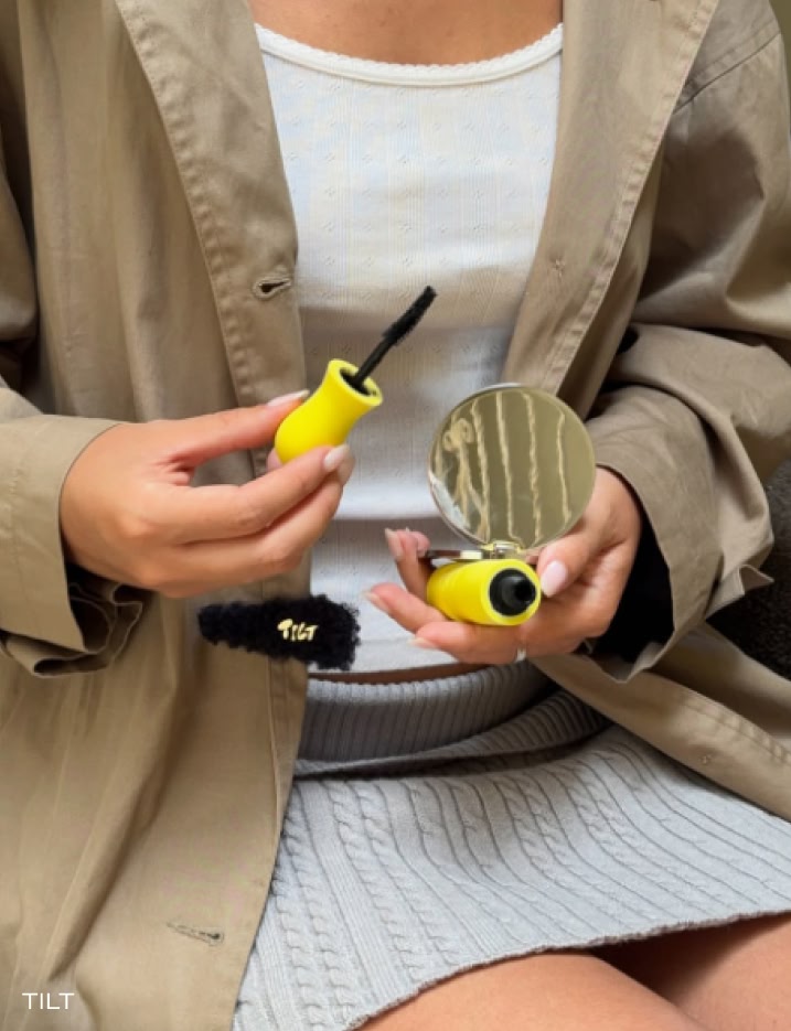 Model holding a mirror and Tilt Beauty Lashscape Lengthening Mascara.