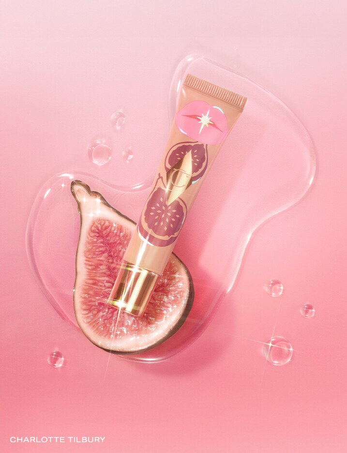 One container of Charlotte Tilbury Unreal Lips Healthy Glow Nectar Oil in shade Candy Fig on top of half a fig.