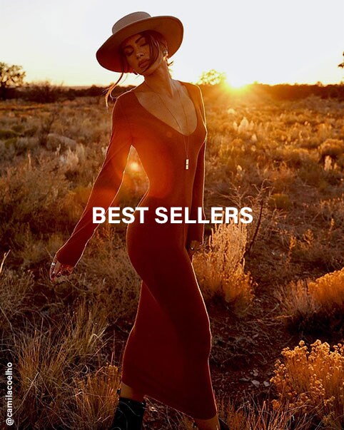 Camila Coelho standing in an open field wearing a brown long sleeve, sweater maxi dress, with a beige hat and brown boots.