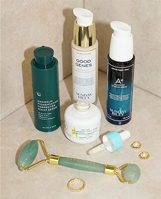 A collection of beauty products displayed next to a jade roller and gold rings. The Beauty Shop. Shop Now.