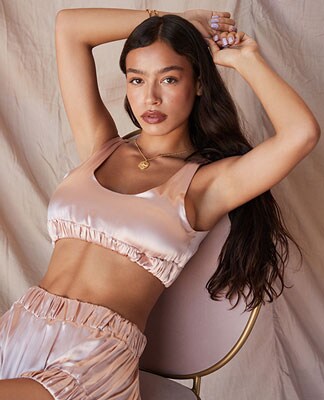 A model is sitting in a chair wearing a satiny pink bra top and matching lounge shorts. Loungewear, But Make It Chic. Shop the edit.