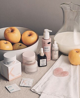An assortment of beauty products displayed next to fruit. The Beauty Shop. Shop Now.