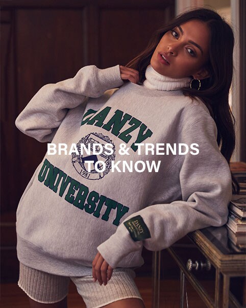 A model leaning over a dresser wearing a red long sleeve crop top with ring cut-out and a matching high waisted midi skirt with side slit, and carrying a beaded clutch. A model wearing a white turtleneck, a grey and green graphic print sweatshirt, and white ribbed biker shorts. A model leaning in a doorway wearing a red long sleeve maxi dress with front shoulder cut-outs, and black heels. A model wearing a blue frayed long sleeve crop top and high waisted blue jeans. Brands & Trends to Know. Shop the Edit.