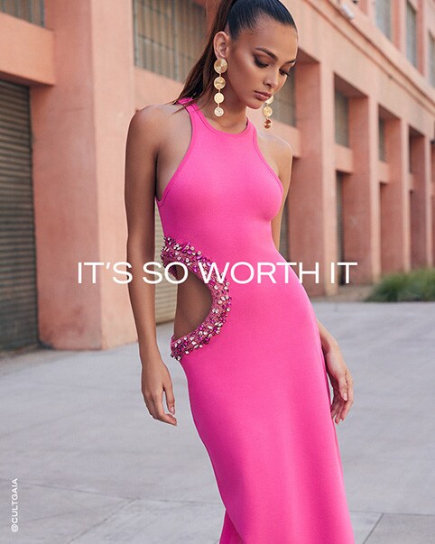 Two photos of a model wearing a bright pink maxi dress that features a high scoop neck and a large cutout on one side of the dress, which is outlined with white and varying shades of pink crystal embellishments. She is also wearing a pair of dangle gold earrings that feature four circles going from big to small. It’s So Worth It. Shop the Edit.