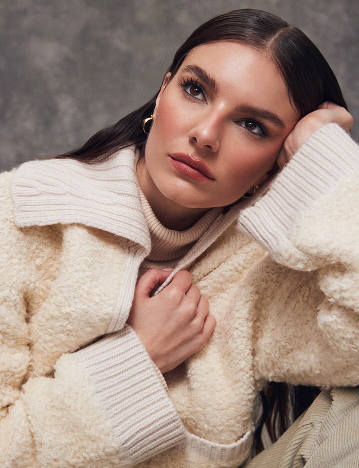 Model with natural makeup wearing a knit and sherpa sweater.