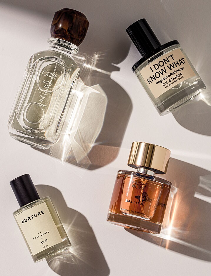 Bottles of perfumes lay on their side over a white surface with a warm light refracting through the glass and amber colored bottles creating shadows and bright angular highlights on the white surface.  