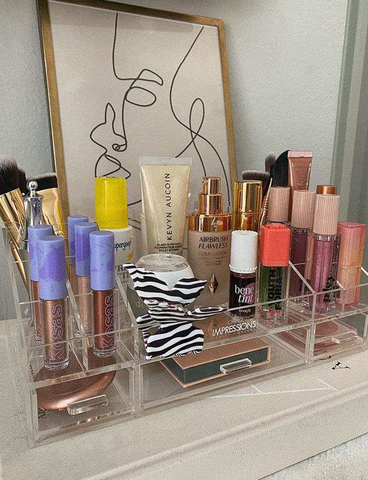 A clear plastic organizer box with separated compartments holds multiple makeup and skincare products. 