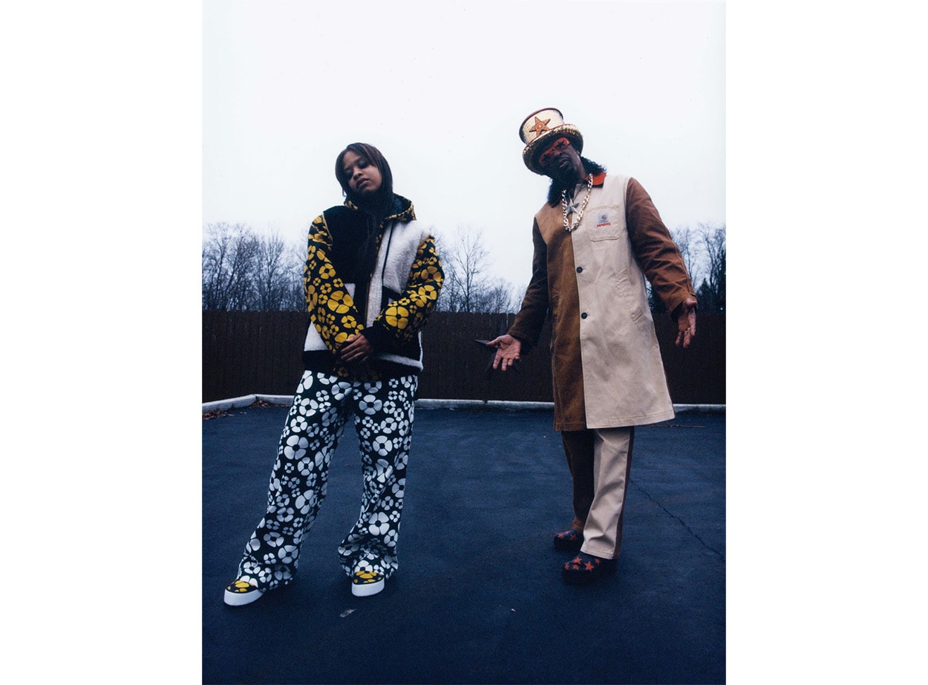 Two models standing side by side wearing Marni x Carhartt outerwear. Left: Jacket and pants with yellow and white floral print. Right: Two-toned brown coat and pants.
