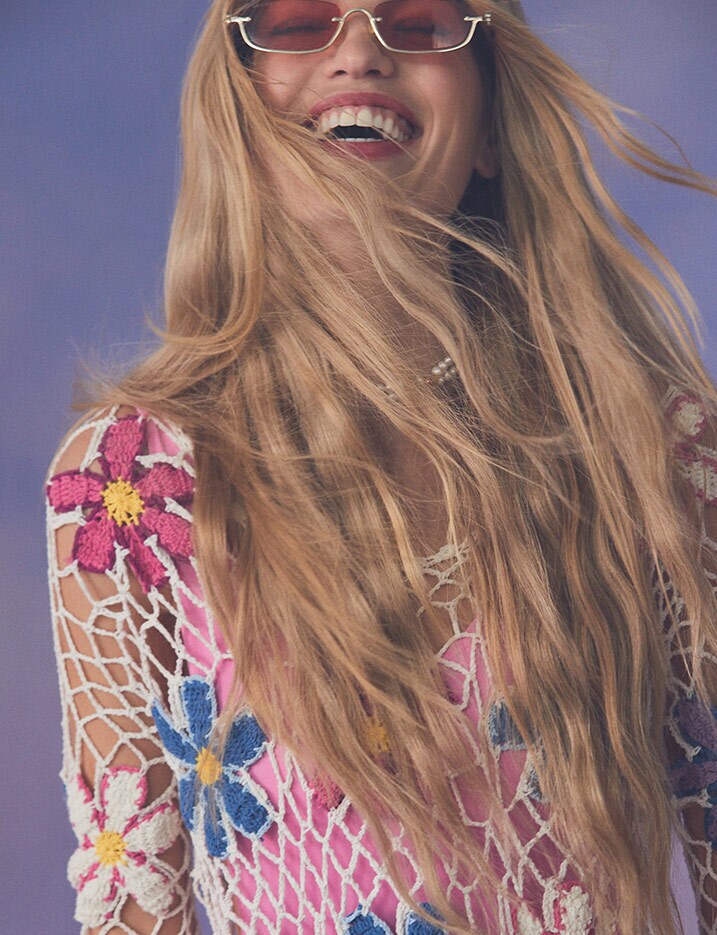 Smiling model with flowing hair wearing a floral mesh cover up in pink and blue