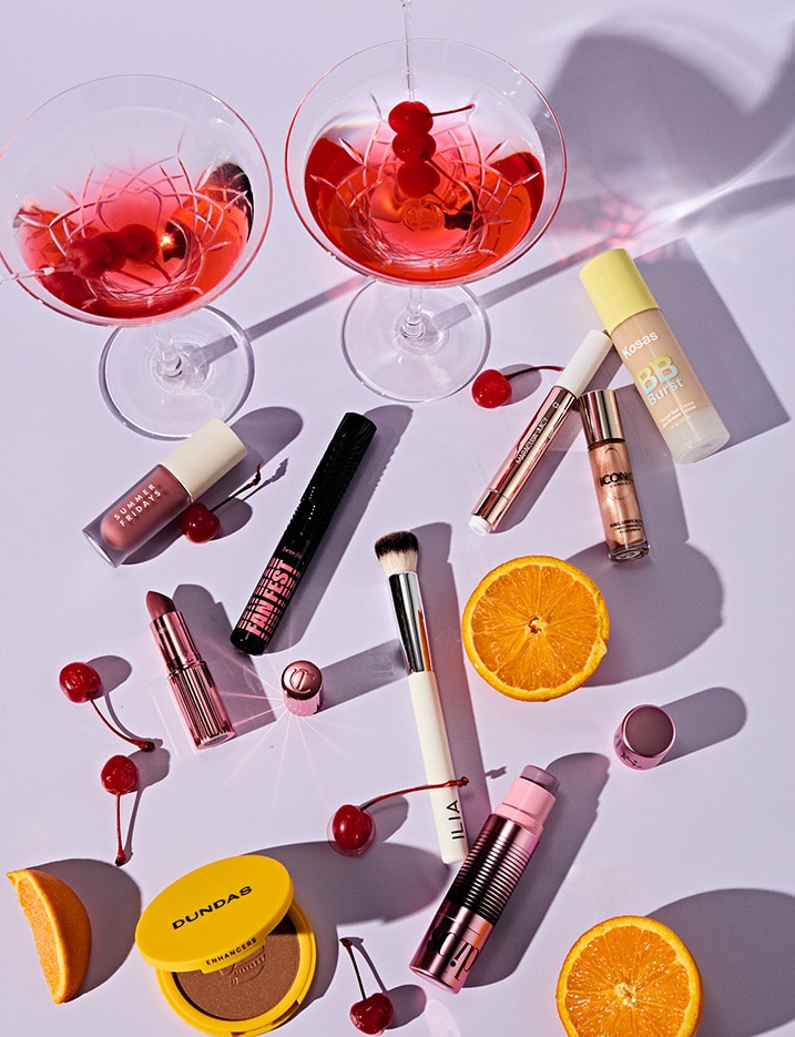 Variety of makeup products arranged with fruit and cocktails.