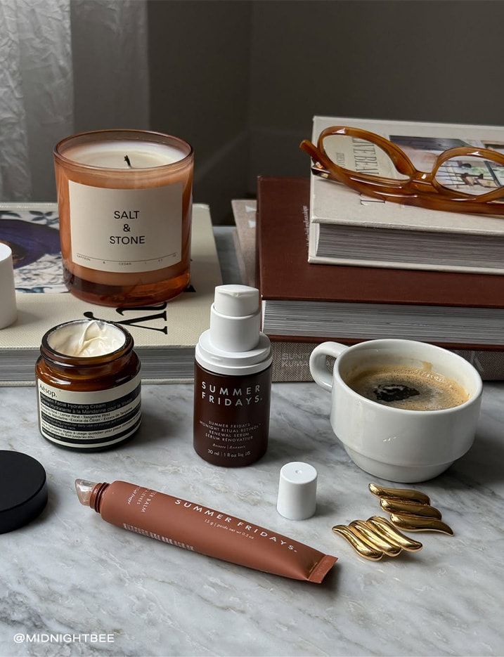 Variety of makeup products next to a cup of coffee and books.