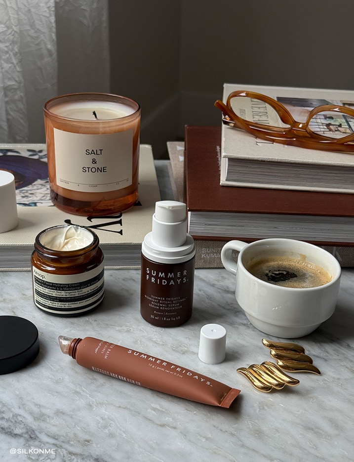 Variety of makeup products next to a cup of coffee and books.