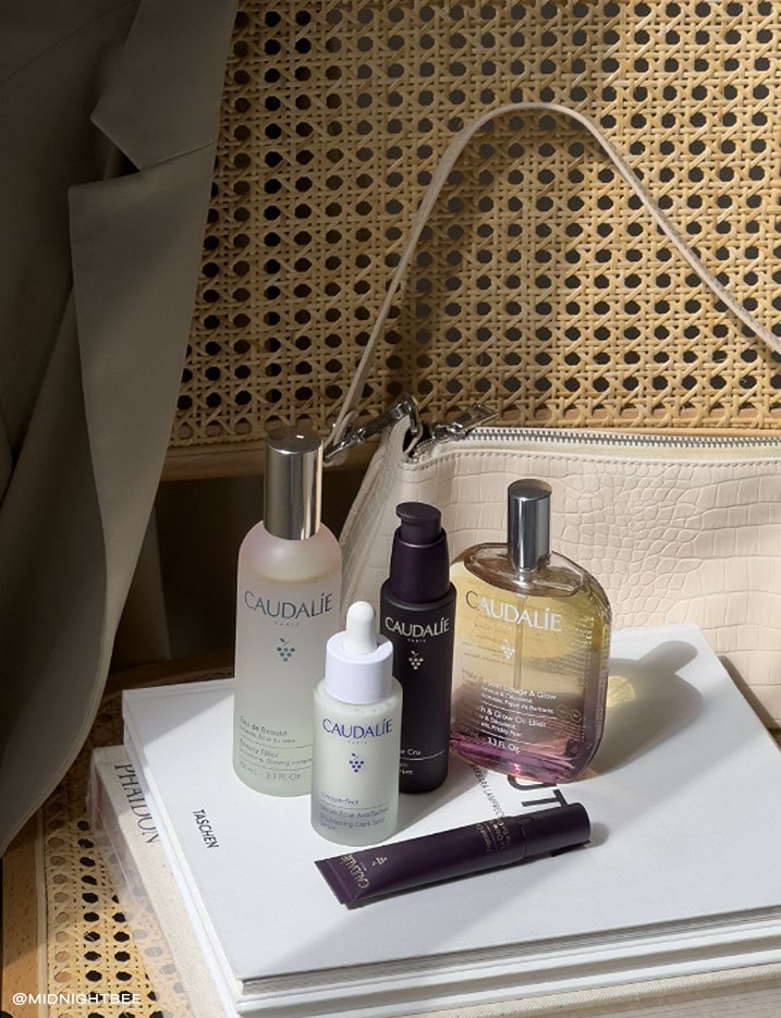 A variety of Caudalie skincare next to a purse.