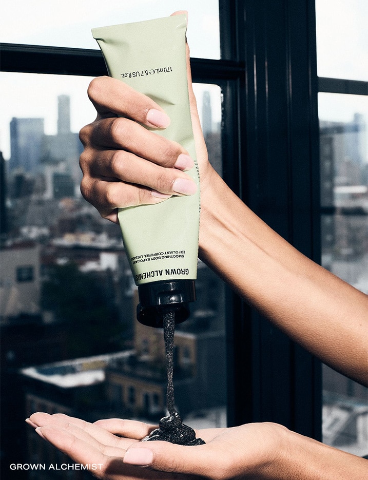 Model squeezing a container of Grown Alchemist Smoothing Body Exfoliant onto hand.
