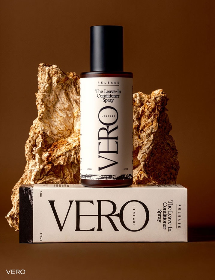 A container of Vero The Leave-In Conditioner Spray on top of its container in front of a rock.