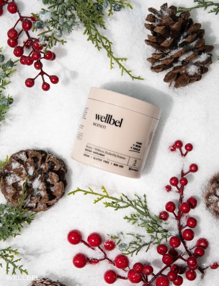 Container of wellbel supplements on the snow surrounded by pine cones and mistletoes.