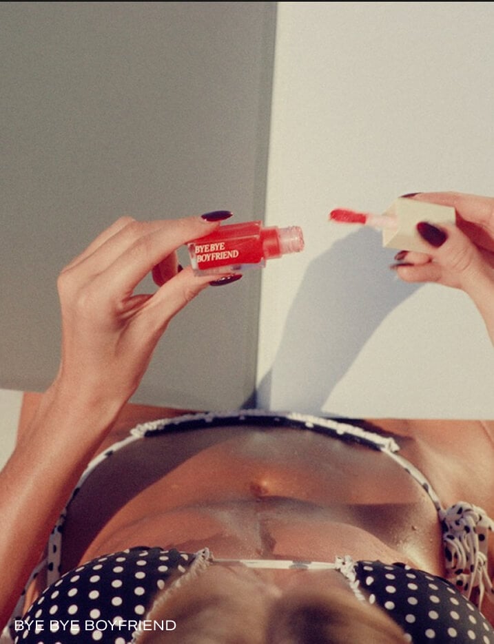 Model pulling the BYE BYE BOYFRIEND lip gloss wand from application bottle.