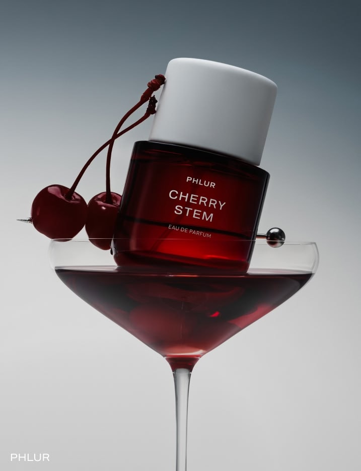 A bottle of Cherry Stem Phlur perfume in a martini glass with a cherry
.