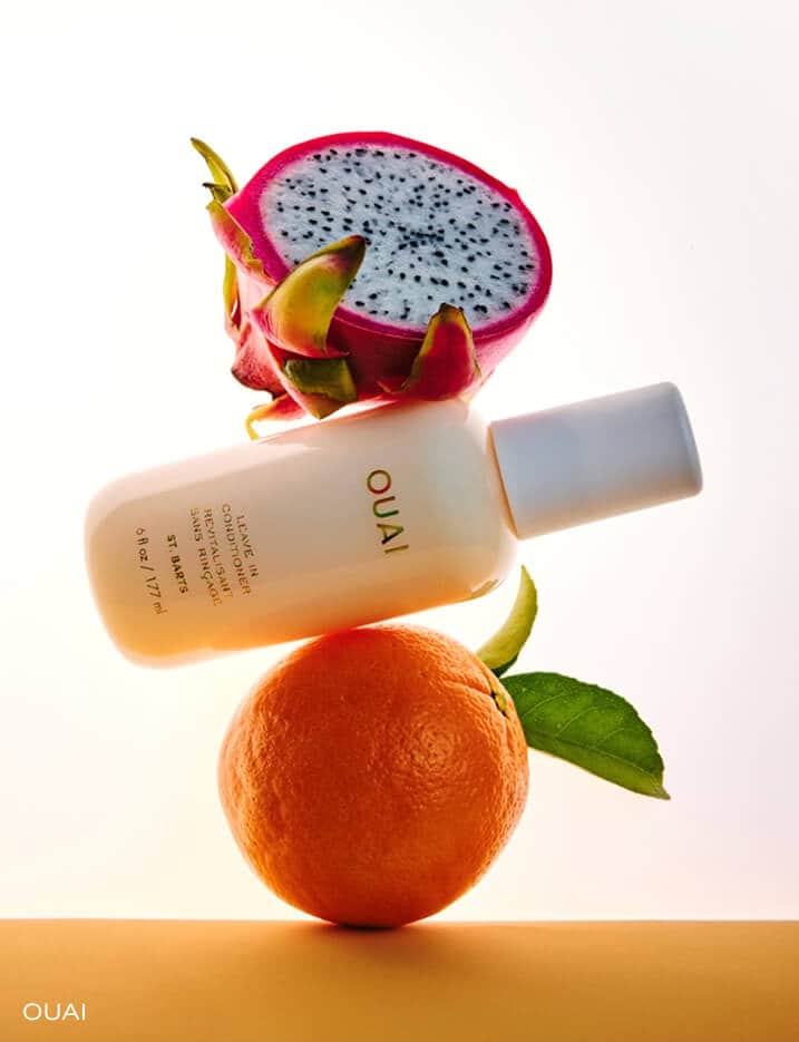 A bottle of Quai haircare with flowers and orange peels.