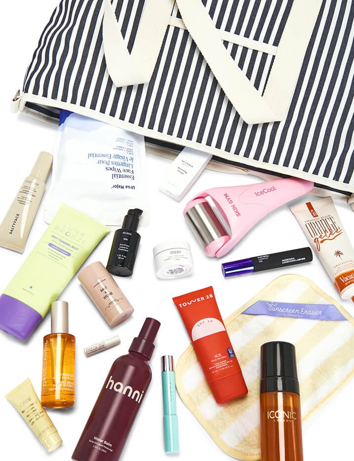 A striped beach bag spilling out the beauty product contents of the REVOLVE Beauty Summer Bag.