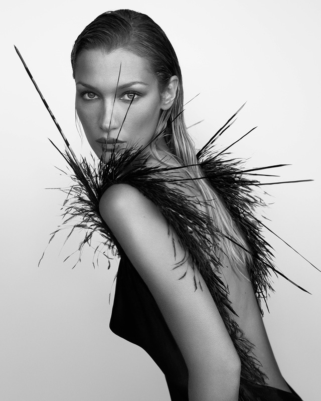 model bella hadid in black and white in a feather adorned backless gown looking over her left shoulder at the camera