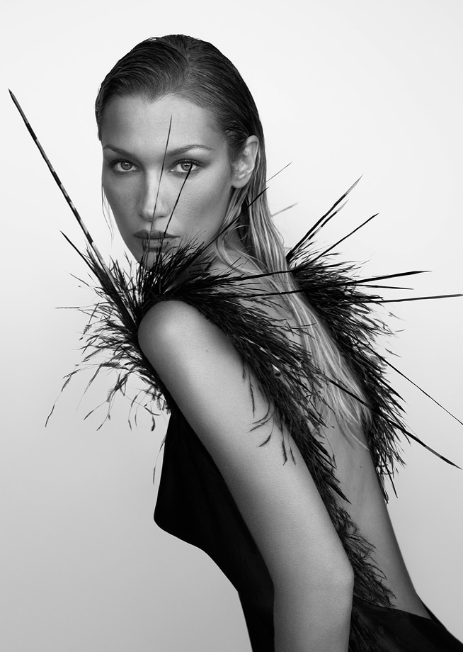 model bella hadid in black and white in a feather adorned backless gown looking over her left shoulder at the camera